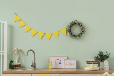Yeşil duvarın yanında çelenk, çelenk ve Paskalya tavşanları olan neşeli mutfağın içi.