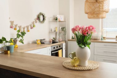 Paskalya çelengi, çelenk, bebek tavuk ve çiçekli bir mutfak tezgahı.