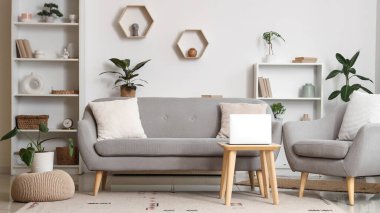 Aydınlık oturma odasının içinde gri kanepe, koltuk ve dizüstü bilgisayarı olan masa.