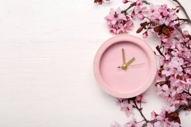 Çiçekli bahar dalları ve beyaz ahşap arka plandaki saat