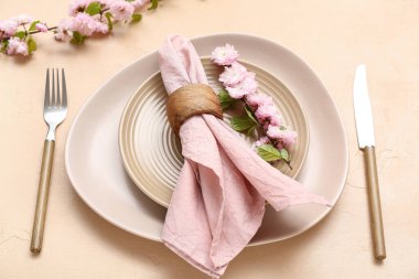 Çatal bıçak takımı, çiçek açan ağaç dalları ve bej arka planda katlanmış peçeteyle servis edilen güzel bir masa.