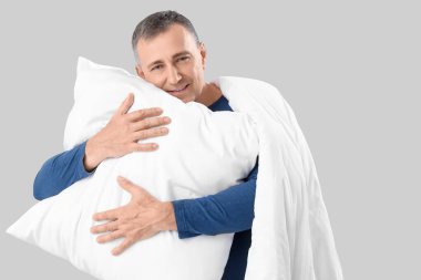 Gri arka planda yumuşak yastıklı ve battaniyeli olgun bir adam.