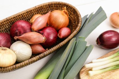 Tahta ve hasır sepette beyaz ahşap arka planda farklı türde soğan var.