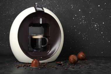 Bir fincan espresso, kapsül kahve makinesi ve siyah grunge masasında fasulye.