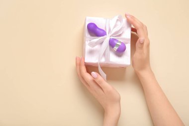 Bej arka planda hediye kutusu ve vibratörü olan kadın elleri.