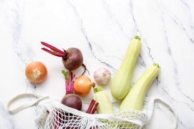 Açık arkaplanda farklı taze sebzeler bulunan ağ torbası.