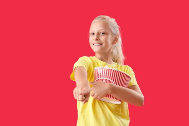 Kırmızı arka plandaki izleyiciyi gösteren patlamış mısırlı mutlu kız.