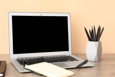 Modern dizüstü bilgisayar, not defterleri ve masasında farklı kalemler olan tutucu.