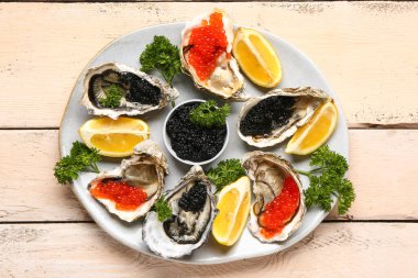 Limonlu lezzetli istiridye tabağı, açık ahşap arka planda siyah ve kırmızı havyar