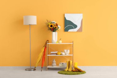 Sonbahar çiçekleri, balkabakları ve turuncu duvarın yanında dekor olan raf ünitesi.