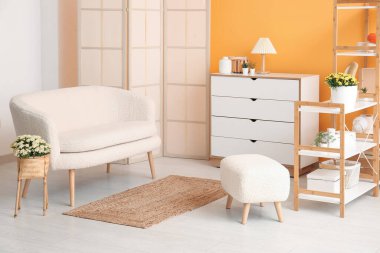 Beyaz kanepe ve hasırdan vazoda kasımpatı çiçekleri olan şık bir oturma odası.