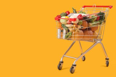 Sarı arka planda yiyecek dolu alışveriş arabası.