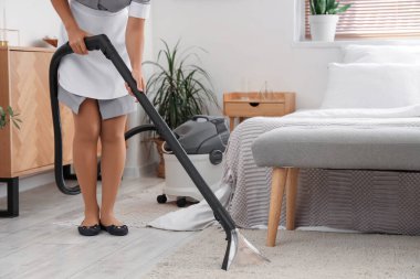 Oda hizmetçisi otel odasını elektrikli süpürgeyle temizliyor.