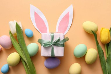 Hediye kutusuyla boyanmış Paskalya yumurtaları, lale çiçekleri ve bej arka planda kağıt tavşan kulakları.