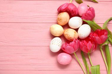 Boyalı Paskalya yumurtaları ve pembe ahşap arka planda güzel lale çiçekleri.