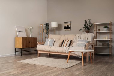 Oturma odasında raf ünitesi ve çiçekleri olan rahat bej kanepe.