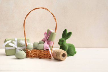 Boyanmış Paskalya yumurtaları, hediye kutuları ve beyaz ahşap masada oyuncak tavşancıklarla dolu bir sepet.