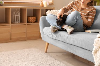 Modern oturma odasındaki kanepede oturan sevimli siyah kedili kadın.