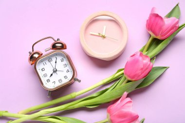 Mor arka planda lale çiçekleri olan farklı çalar saatler.