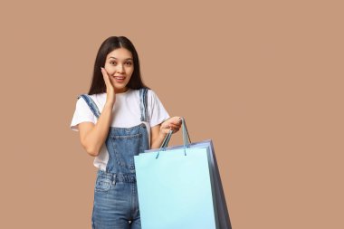 Kahverengi arka planda alışveriş torbaları olan şık kot pantolonlu Asyalı bir kadın.