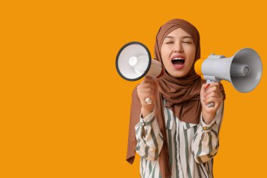 Genç Asyalı Müslüman kadın sarı arka planda megafonlara bağırıyor. Ulusal Duyulma Günü