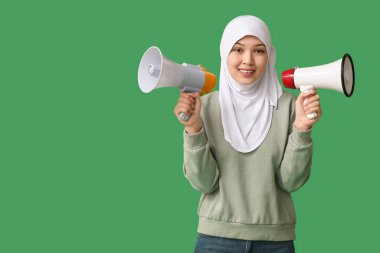 Yeşil arka planda megafonları olan genç Asyalı Müslüman kadın. Ulusal Duyulma Günü