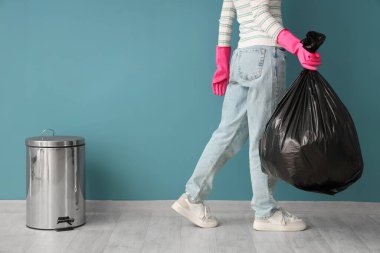 Woman with garbage bag and trash bin near blue wall