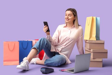 Cep telefonu ve dizüstü bilgisayarı olan genç bir kadın eflatun arkaplanından alışveriş yapıyor.