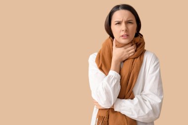 Kahverengi arka planda boğazı ağrıyan fularlı güzel bir kadın.