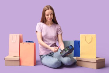 Kredi kartlı genç bir kadın. Leylak arka planındaki terminalden alımlarını karşılıyor.