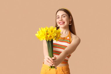 Kahverengi arka planda bir buket nergis çiçeğiyle mutlu genç bir kadın.