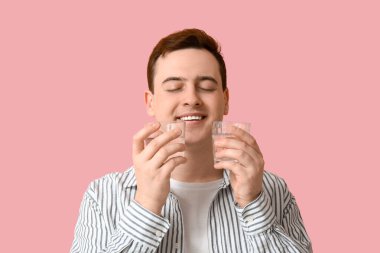 Pembe arka planda temiz su bardakları olan yakışıklı bir genç.