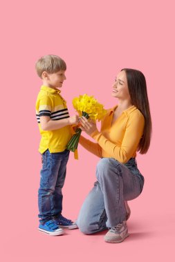 Oğlum pembe arka planda oturan mutlu annesine bir buket narsisle selam veriyor.
