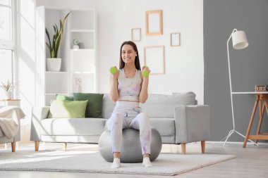 Spor yapan genç bir kadın, evde halterle spor yapıyor.