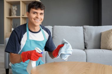 Young man cleaning coffee table at home