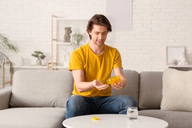 Evdeki kanepede oturan balık yağı kapsülleri ve su dolu kavanozu olan yakışıklı genç adam.