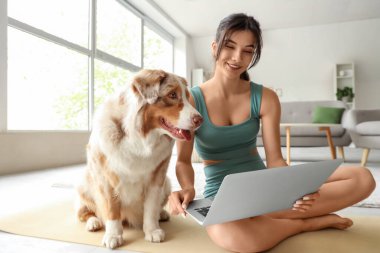 Evde dizüstü bilgisayar kullanan Avustralyalı çoban köpeği olan genç bir kadın.