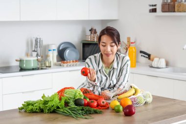 Mutfakta meyve ve sebzeli domatesli genç bir Asyalı kadın.