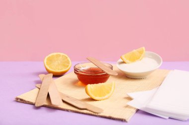 Şekerleme macunu, balmumu şeritleri, ahşap çubuklar ve renkli arkaplanlı limon kasesi.