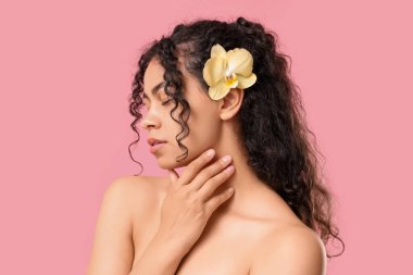 Pembe arka planda sarı orkide çiçeğiyle güzel bir Afro-Amerikalı kadın.