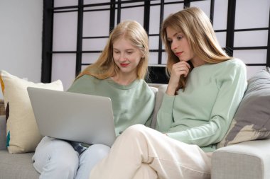 Evdeki kanepede dizüstü bilgisayarı olan güzel, mutlu kız kardeşler.