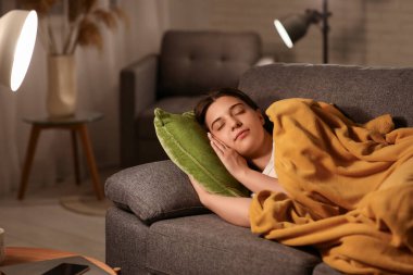 Pijamalı genç bir kadın. Ekoseli. Geceleri oturma odasında rahat bir kanepede uyuyor.