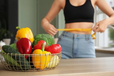 Mutfakta mezurası ve bir sepet taze sebzesi olan güzel genç bir kadın, yakın plan. Kilo verme konsepti