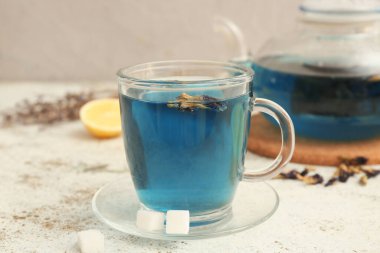 Bir fincan kelebek çiçeği çayı, çay tabağı ve şeker arkaplanda, yakın plan.