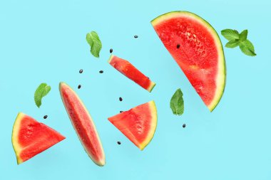 Uçan taze karpuz parçaları ve mavi arka planda nane ve tohumlar.