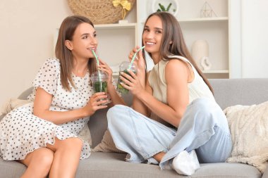 Evdeki kanepede oturan bir bardak mojito ile güzel, genç ve mutlu kadınlar.
