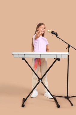 Sentezleyici ve mikrofonlu küçük kız bej arka planda şarkı söylüyor.