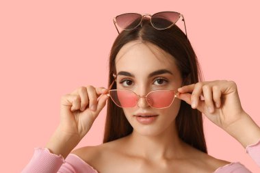 Pembe arka planda farklı tarz güneş gözlüklü güzel bir genç kadın.