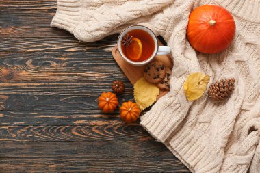 Bir fincan çay, sıcak süveter, mumlar ve koyu ahşap arka planda sonbahar dekoru ile kompozisyon