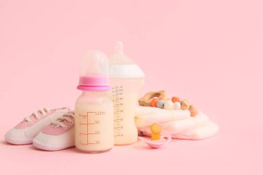 Bebek sütü formülü, patik, emzik, ip ve pembe arka planda bebek bezi olan şişeler.